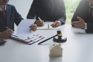 Equipo de abogados discutiendo documentos en una mesa con un mazo y una maqueta de casa, simbolizando asesoría legal en bienes raíces.
